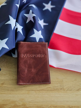 Details of a passport holder placed on an American flag alongside the stars and stripes in a flat lay arrangementの写真素材