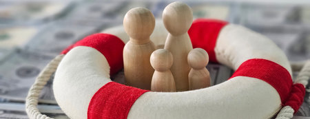 A lifebuoy surrounds wooden figures representing family on a backdrop of hundred-dollar bills conveying financial safety and securityの写真素材