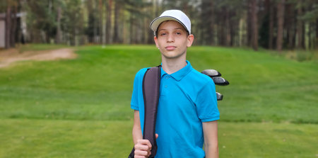 Young golfer ready to play on a lush green course with tall trees in the background during a calm afternoonの写真素材