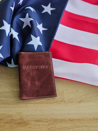 Red and blue fabric with stars and stripes is placed on a wooden surface with a brown passport coverの写真素材