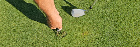 A golfer repairs the greens at a single golf course in the afternoon, paying special attention to...