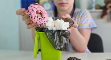 A child plans to throw a donut in a trash can filled with sugar cubes. The harm of sweets for...
