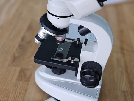Microscope on wooden table showing sample stage and objective lenses for biology studies in a lab...