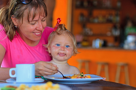 young mother feeding infant daughter in cafeの写真素材