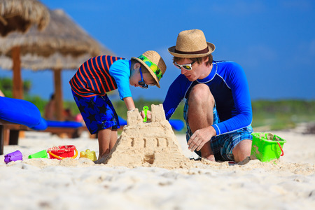 father and son building sand castle on tropical sand beachの写真素材