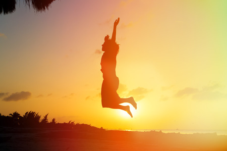 Silhouette of woman jumping on sunset beach