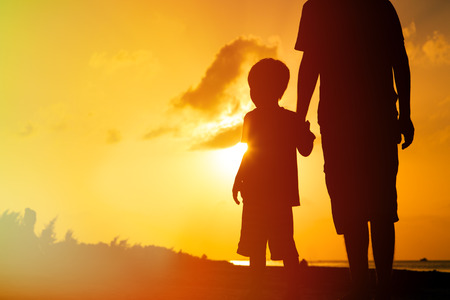 silhouette of father and son holding hands at sunset seaの写真素材