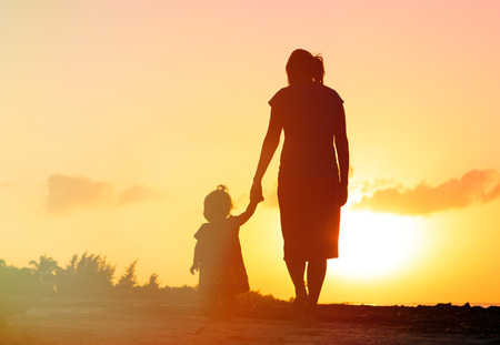 mother and little daughter walking on the beach at sunsetの写真素材