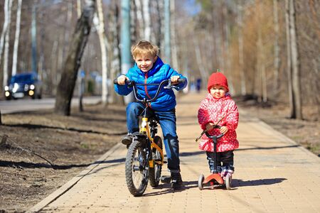 little boy and toddler girl, brother and sister, riding bicycle and scooter outdoorsの写真素材