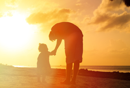 silhouettes of father and little daughter walking on beach at sunsetの写真素材