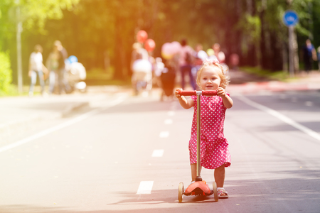 happy cute little girl learning to ride scooter in the cityの写真素材