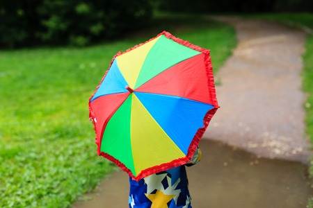 little boy hiding behind colorful umbrella outdoors on rainy dayの写真素材