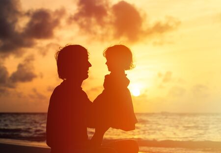 Father and little daughter silhouettes on beach at sunsetの写真素材