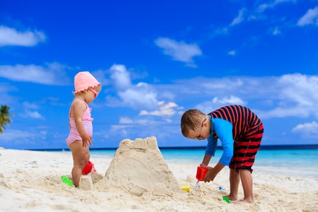 little boy and toddler girl building sandcastle on summer beachの写真素材