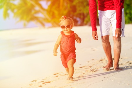 father and little daughter walking on summer tropical beach