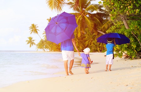 Father and two kids at beach with umbrellas to hide from sunの写真素材