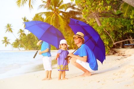 Father and two kids at beach with umbrellas to hide from sunの写真素材