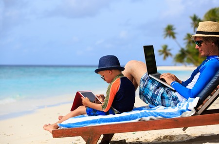 father and son with laptop and touch pad on summer beachの写真素材
