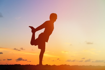 Silhouette of young man doing yoga at sunset beachの写真素材