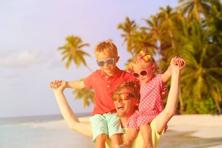 happy father with two kids on shoulders having fun at tropical beachの写真素材