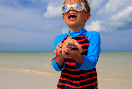 little boy holding seashells on summer tropical beachの写真素材