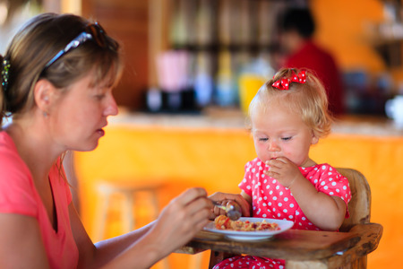 young mother feeding infant daughter in cafeの写真素材