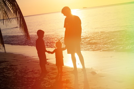 father and two kids walking on beach at sunsetの写真素材