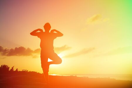 Silhouette of young man doing yoga at sunset beachの写真素材