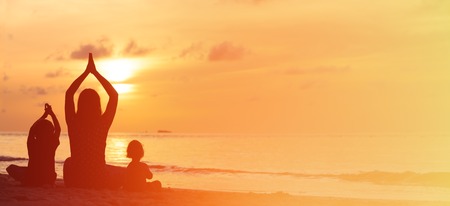 silhouette of mother and kids doing yoga at sunset, panoramaの写真素材