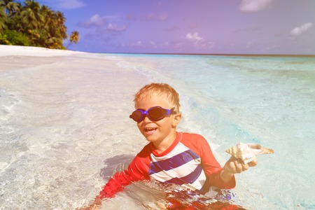 little boy swimming holding shell on tropical beachの写真素材