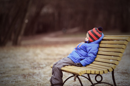 lonely child sitting on bench in park, winter depressionの写真素材