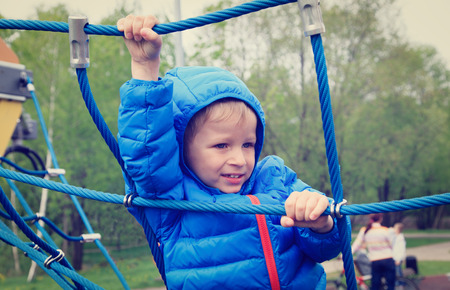 little boy climbing rope on the playground outdoorsの写真素材