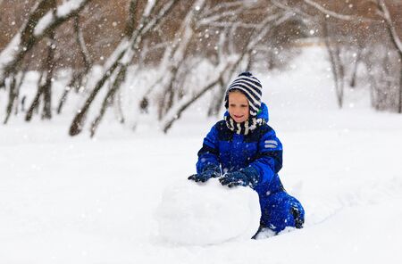 cute little boy building snowman in winter parkの写真素材