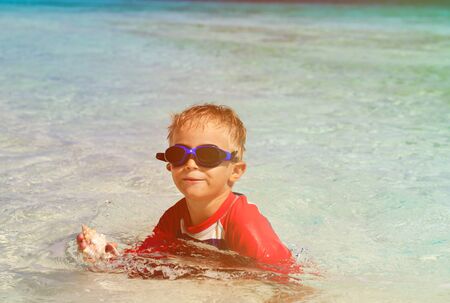 little boy swimming holding shell on tropical beachの写真素材