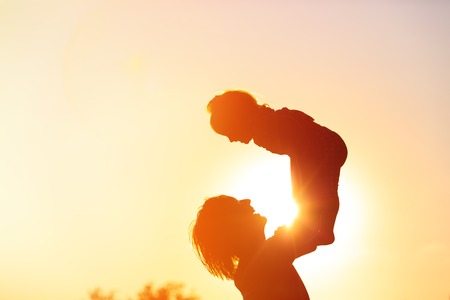 silhouettes of father and little daughter playing at sunset skyの写真素材