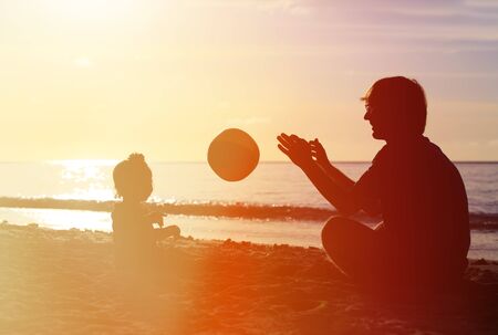 silhouette of father and little daugther play ball on sunset beachの写真素材