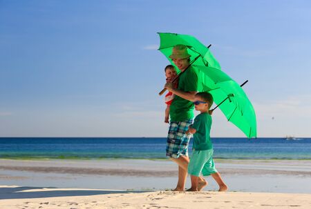father and kids with umbrellas on tropical beach vacationの写真素材