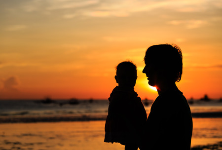 Father and little daughter silhouettes on beach at sunsetの写真素材