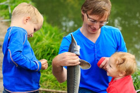 father and two kids holding fish they caught on the lakeの写真素材