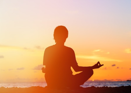 Silhouette of young man meditating at sunset beachの写真素材