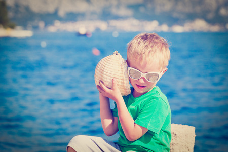 little boy listening seashell at the beach, summer vacationの写真素材