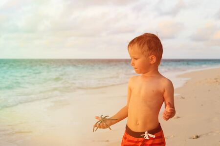 little boy holding starfish on tropical sunset beachの写真素材