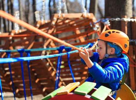 little boy climbing in adventure activity park with helmet and safety equipment