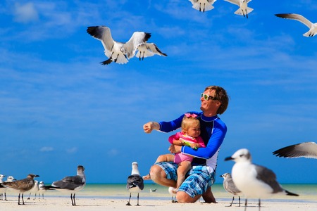 father and little daugther feeding seagulls on summer beachの写真素材