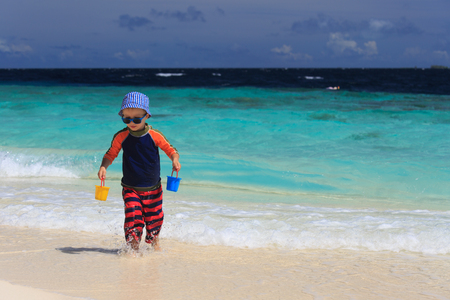 little boy playing with water on tropical sand beachの写真素材