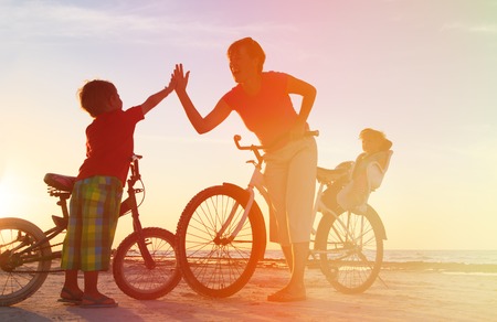 happy mother with kids biking at sunset beachの写真素材