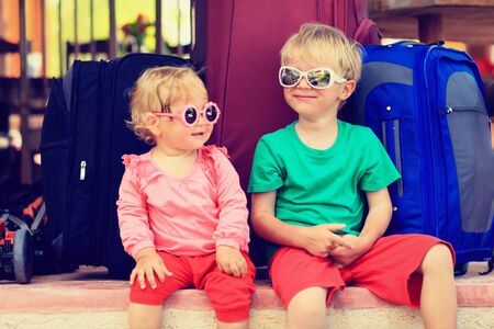 little boy and toddler girl sitting on suitcases ready to travel, kids travel conceptの写真素材