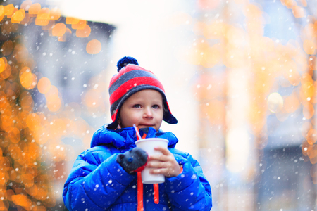little boy having hot drink in cold winter christmas cityの写真素材
