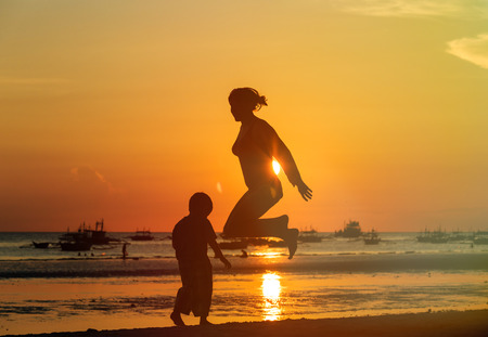 happy mother and son jumping at sunset beachの写真素材