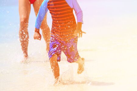 little boy with mother playing with water on tropical beachの写真素材